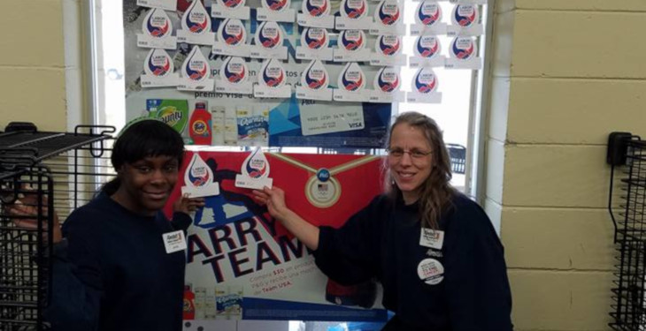 two workers stand in front of cancer fundraising wall to show donations from customers.